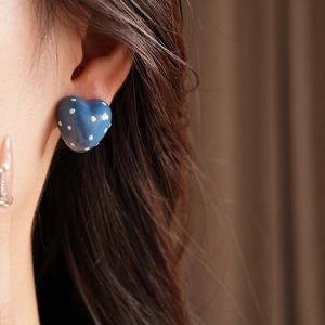 Close-up of blue heart-shaped earrings with white polka dots worn by a model