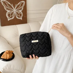 Detailed macro of a black quilted heart makeup bag with a gold logo tag