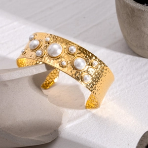Golden hammered texture cuff bracelet with white pearl inlays on a stone pedestal