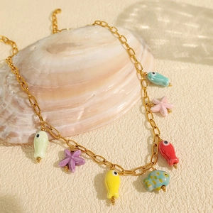 Gold ocean necklace with colorful ceramic starfish and fish pendants on a seashell background