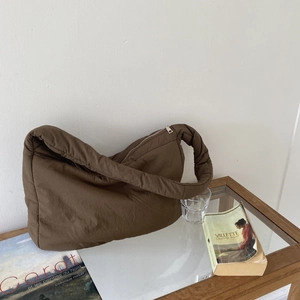 Detail view of a brown padded nylon tote bag with a unique twisted strap on a glass table
