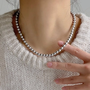 Close-up of elegant silver beaded necklace worn on a model with beige knit sweater