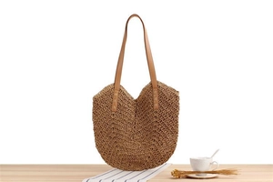 Detail of hand-woven straw tote bag with brown leather straps on a wooden surface