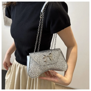 Detail of silver sequin bag with metal bow accent and chain strap worn by a model