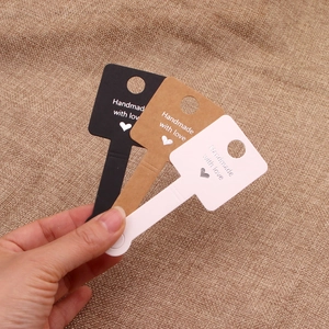 Key-shaped handmade jewelry tags in black, kraft, and white held over burlap