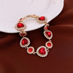 Détail du bracelet doré avec pierres rouges en cœur et rondes sur assiette blanche
