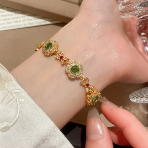 Detail of 24K gold plated flower bracelet with green square gemstones and red butterfly charms