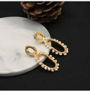 Detail shot of gold oval-frame earrings with woven white pearls on a marble base