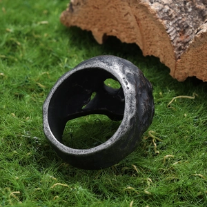 Close-up of vintage pirate skull ring with hammered texture on a rustic moss background