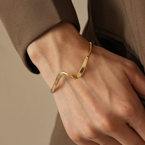 Detailed view of an irregular wavy gold bracelet on a wrist against a brown blazer