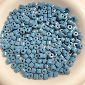 Dettaglio di perline cilindriche blu da 6mm in una ciotola bianca per gioielli fai da te
