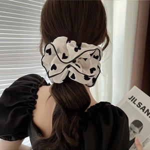 Detail of white chiffon scrunchie with black heart pattern worn on model wrist