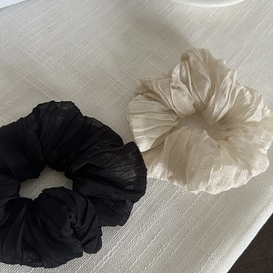 Ensemble de grands chouchous plissés noirs et blanc crème sur un fond en tissu texturé