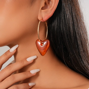 Macro detail of amber resin heart pendant on golden hoop earrings worn by a model