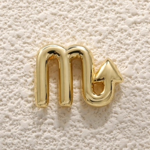 Detailed view of a gold-plated Scorpio zodiac pendant on a white textured background