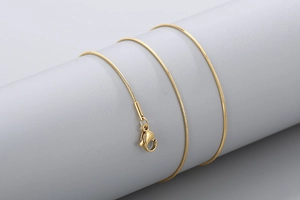 Macro shot of glossy gold snake chain necklace with lobster clasp on grey stand