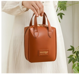 Brown PU leather shell makeup bag with handles and logo detail shown in hand