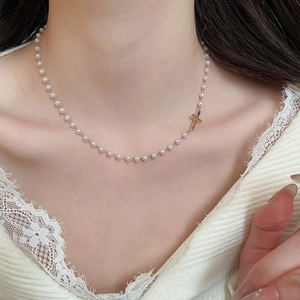 Close-up of pearl necklace with gold cross pendant worn by model on lace fabric