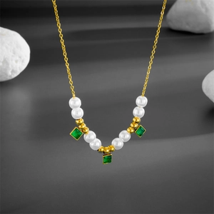 Detail of beaded gold chain necklace featuring green square gemstones and white pearls