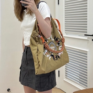 Close-up of olive green nylon bag featuring detailed horse embroidery and braided rope handle