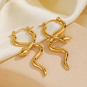 Golden snake-shaped stainless steel earrings on beige stone and white silk background