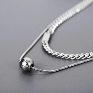 Détail d'un collier double épaisseur en acier titane argenté avec pendentif boule poli