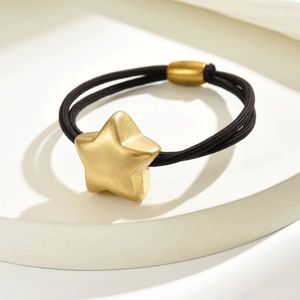 Close-up of a matte gold star pendant on a black high-elastic hair tie on a white stand