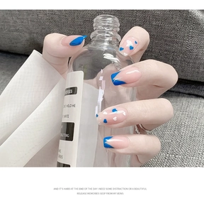 Detail of nude pink press-on nails with blue French tips and heart patterns on hands