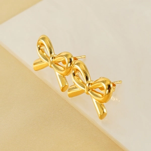 Polished 18K gold titanium steel bow stud earrings displayed on white geometric stands