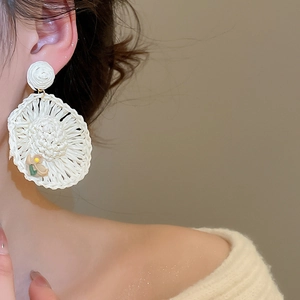 Detail of oversized white raffia sunflower earrings with floral accents for beach vacations