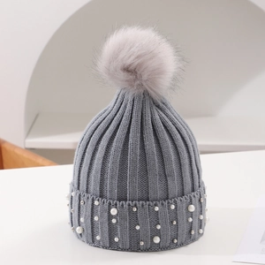 Detail of grey knitted hat featuring pearl embellishments and a large faux fur pom-pom