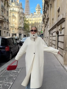 Detailed view of white oversized wool coat with high collar and black buttons on city street