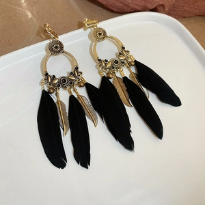 Détail de boucles d'oreilles créoles dorées avec plumes noires et feuilles en métal