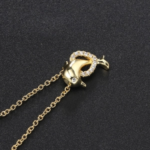 Close-up of golden dolphin pendant with sparkling zircon inlays on a black textured surface