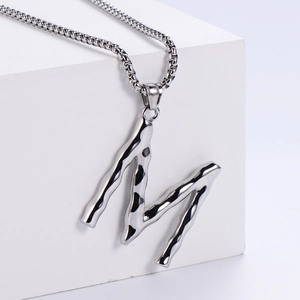 Détails macro de la texture métal liquide sur le pendentif lettre M argenté avec chaîne