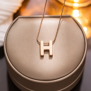 Elegant rose gold titanium H-letter pendant necklace on a jewelry display box