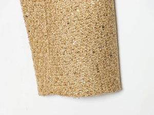 Dettaglio del tessuto in tweed dorato con fili metallici e decorazioni di paillettes