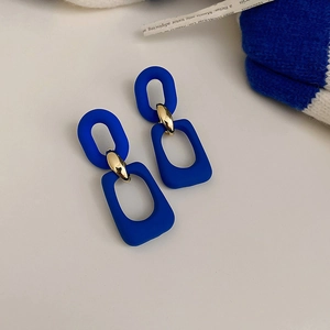 Detail of matte blue geometric link earrings with gold metal accents on white backdrop