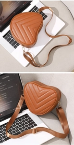 Detail view of heart-shaped brown crossbody bag with V-quilt pattern on a laptop