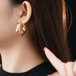 On-ear view of golden irregular crinkle hoop earrings against a dark background