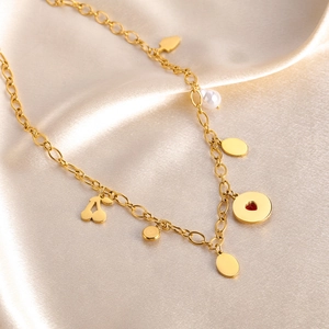 Detail of gold titanium necklace with cherry and heart pendants on silk fabric