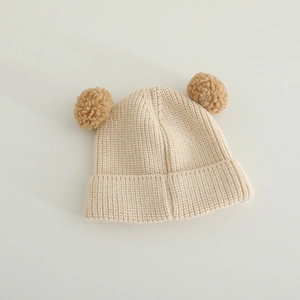 Detail of soft cream knitted baby beanie with fuzzy brown pom-pom bear ears on white