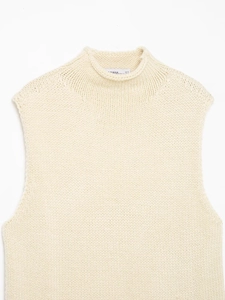 Detail of off-white chunky knit sleeveless vest with high neckline and ribbed texture