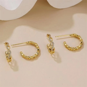 Détail de boucles d'oreilles dorées tressées avec zircons sur fond beige doux