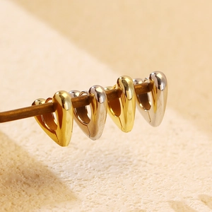 Macro shot of gold and silver S925 heart hoop earrings arranged on a slim rod