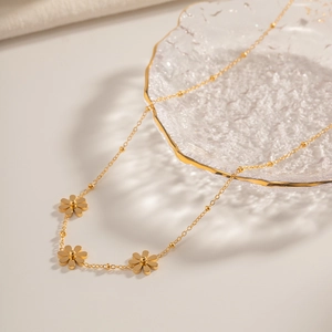 Détail d'un collier marguerite doré présenté sur un plateau en verre texturé
