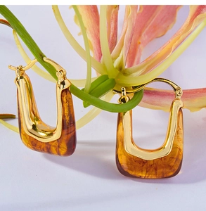 Detailed view of U-shaped gold earrings with amber resin hung on a floral stem