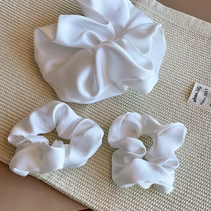 Close-up of three white silk scrunchies in large and small sizes on a woven beige mat