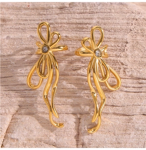 Detailed view of golden ribbon bow earrings featuring a sparkling centered zircon
