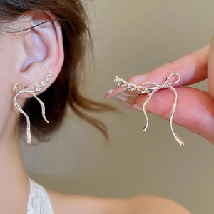 Detail of silver bow tassel earrings shown worn on ear and held in hand for size comparison